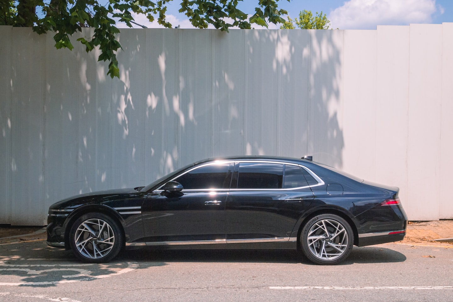 Una berlina di lusso nera parcheggiata all'aperto vicino a un muro di lamiera ondulata.