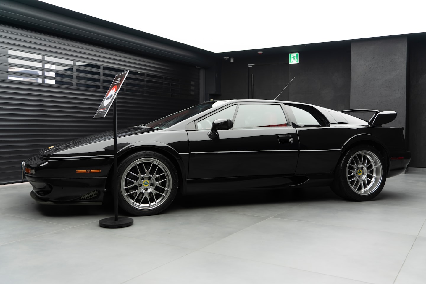 Vettura sportiva nera esposta su un pavimento piastrellato grigio in uno showroom.
